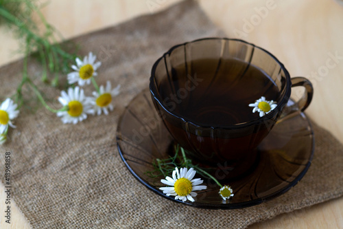 dark glass cup of Herbal tea with chamomile tea on sackcloth on a light wooden table with copy space. cup fo tea with bouquet fresh flowers and green leaves on yellow background. Healthy lifestyle