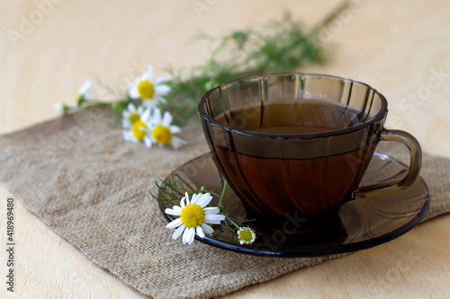 dark glass cup of Herbal tea with chamomile tea on sackcloth on a light wooden table with copy space. cup fo tea with bouquet fresh flowers and green leaves on yellow background