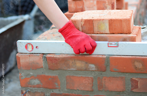 Fotografija Brick masonry: A bricklayer is checking the evenness of a brick wall, brick foundation using a spirit level