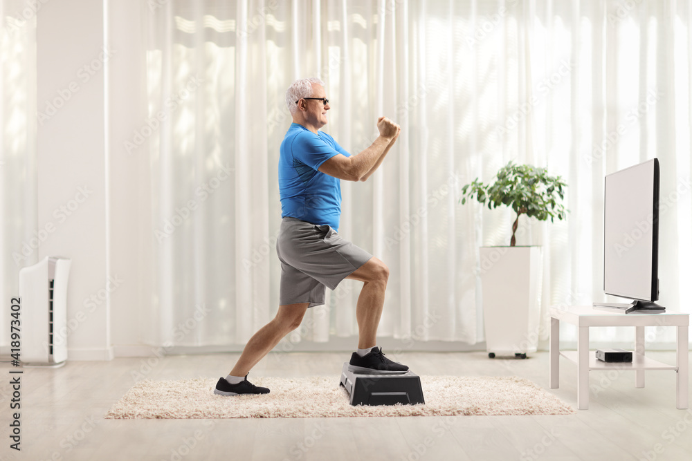 Mature man exercising on a step aerobic platform in front of a tv at home Mature man exercising on a step aerobic platform in front of a tv at home