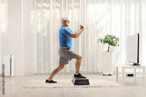 Mature man exercising on a step aerobic platform in front of a tv at home
