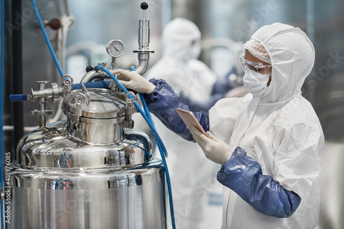 Portrait of female worker wearing protective suit while operating equipment at modern chemical plant, copy space photo