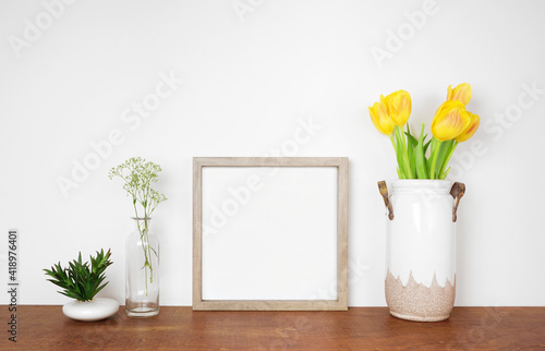 Mock up square wood frame with succulent and spring flowers. Wooden shelf against a white wall. Copy space.