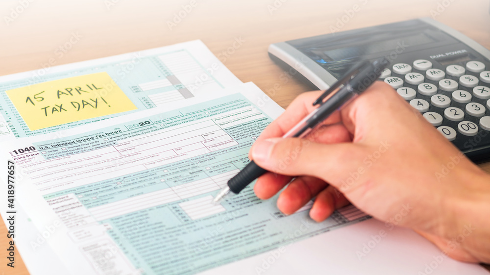 Filling 1040 form on tax day with calculator on table to be returned. American event. Filling 1040 form on tax day with calculator on table to be returned. American event.