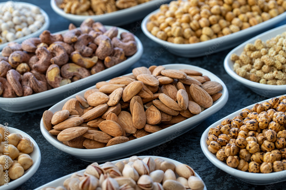 Almond in selective focus. Nuts on plate on a dark background. Walnut, Chickpeas, White Chickpeas, Dry mulberry, almond, cashew, pistachio. Types of nuts on the plate. Almond in selective focus. Nuts on plate on a dark background. Walnut, Chickpeas, White Chickpeas, Dry mulberry, almond, cashew, pistachio. Types of nuts on the plate.