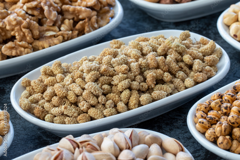 Obraz premium Dry Mulberry in selective focus. Nuts on plate on a dark background. Walnut, Chickpeas, White Chickpeas, Dry mulberry, almond, cashew, pistachio. Types of nuts on the plate.