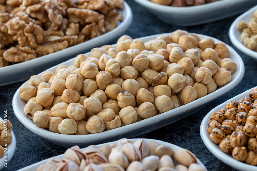 Hazelnuts in selective focus. Nuts on plate on a dark background. Walnut, Chickpeas, White Chickpeas, Dry mulberry, almond, cashew, pistachio. Types of nuts on the plate.