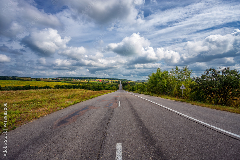 Empty summer highway in a hilly area, on the background of blue sky and white clouds