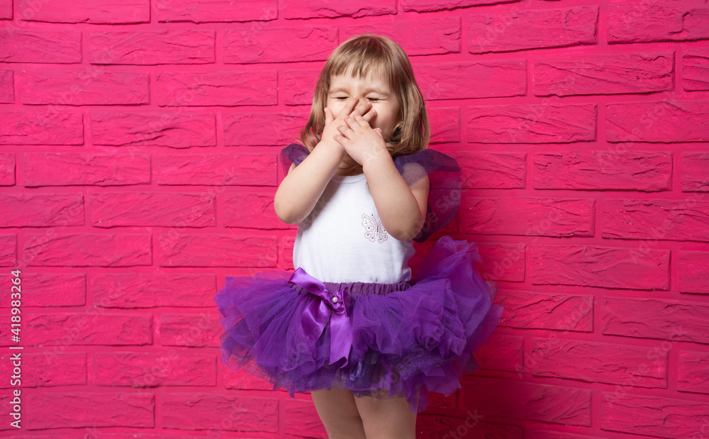 carefree cute little girl in tutu skirt giggling covering her mouth with her hand on pink background. carefree cute little girl in tutu skirt giggling covering her mouth with her hand on pink background.