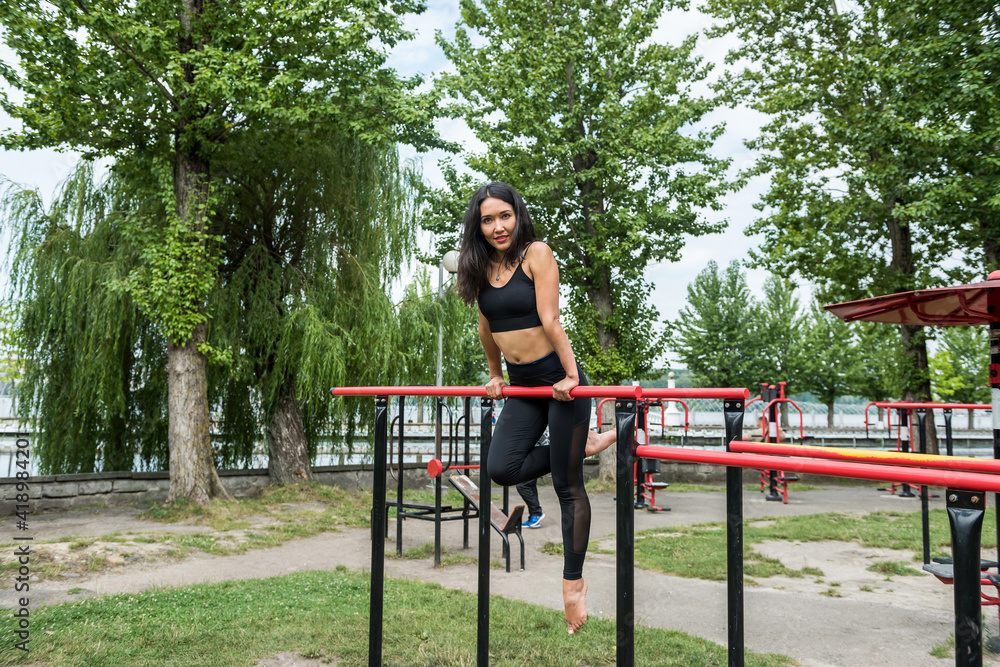 Naklejka premium Young woman doing street workout on the horizontal bar, in summer morning