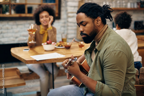 African American man playing acoustic guitar while being with his family at home.
