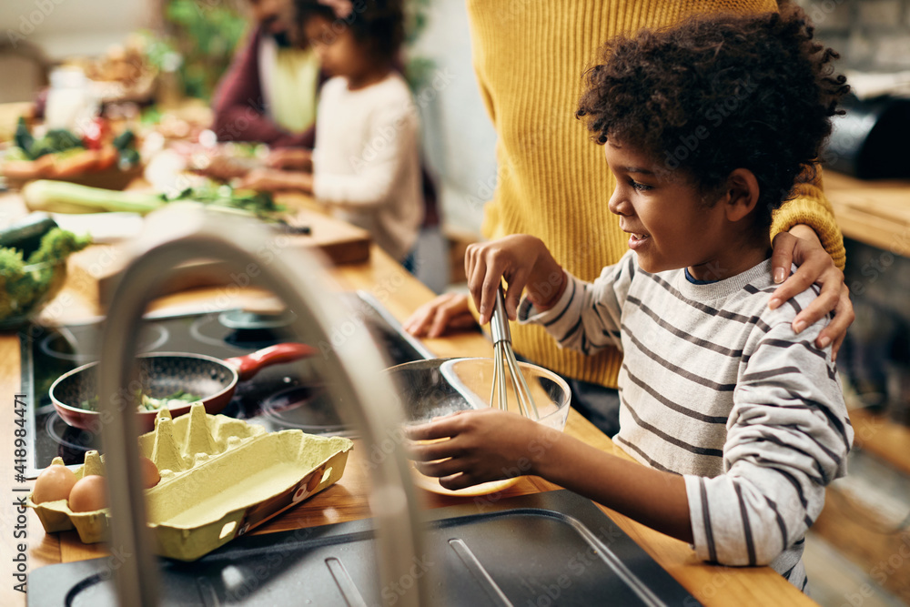 Happy black boy preparing scrambled eggs with his mother in the kitchen. Happy black boy preparing scrambled eggs with his mother in the kitchen.