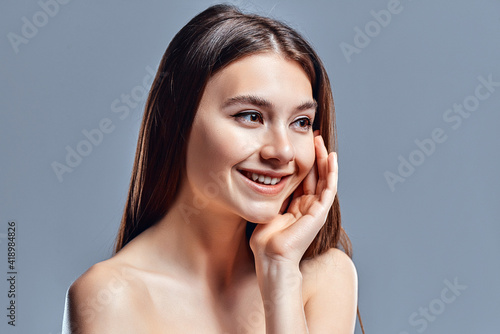 Beautiful young woman with clean perfect skin. Portrait of beauty model with natural nude makeup. Spa, skin care and wellness. Close up, gray background, copyspace.