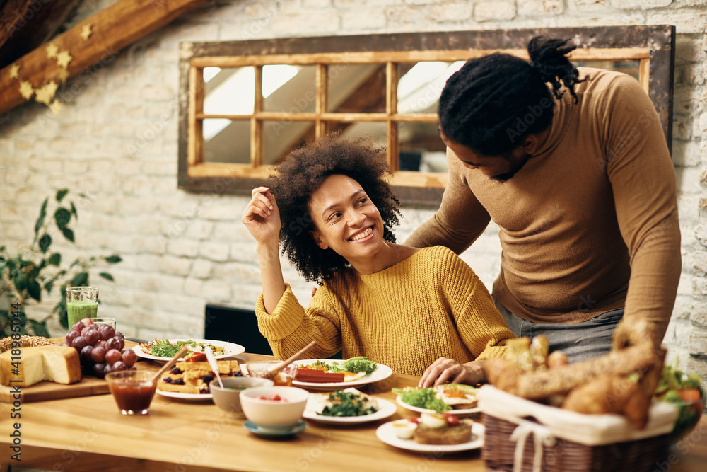 Happy African American couple talking while having meal at dining table ...