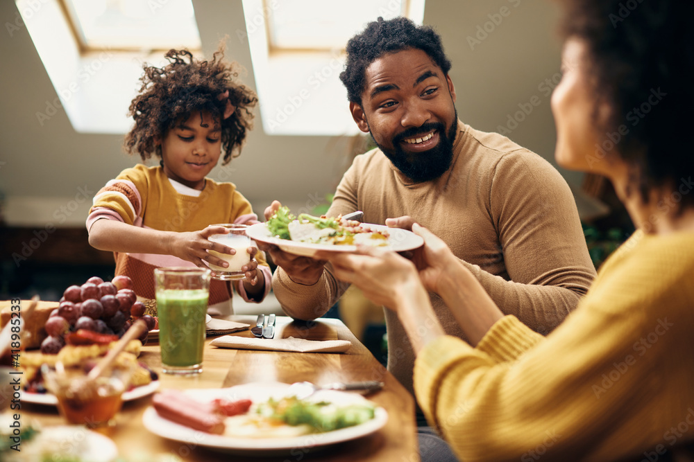 Happy African American man having breakfast with his family at dining table.