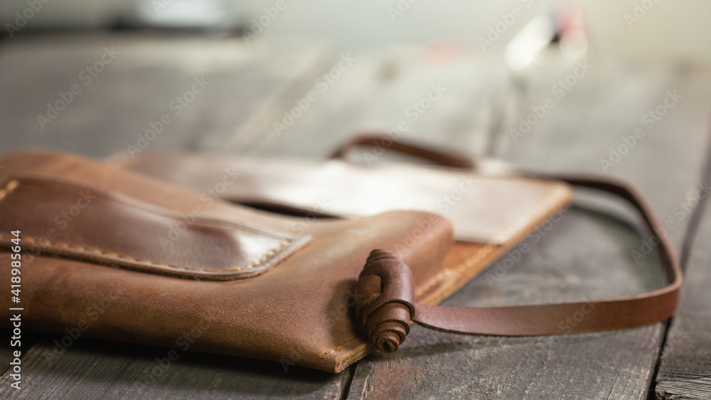 Brown style tobacco pouch leather on wood background. Craft product handmade. Hand sewing.