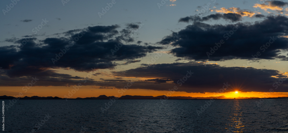 Obraz premium scenic and colorful sunset over the ocean with shimmering light on the waves and silhouette of mountains on the shore behind