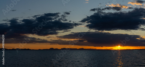 scenic and colorful sunset over the ocean with shimmering light on the waves and silhouette of mountains on the shore behind