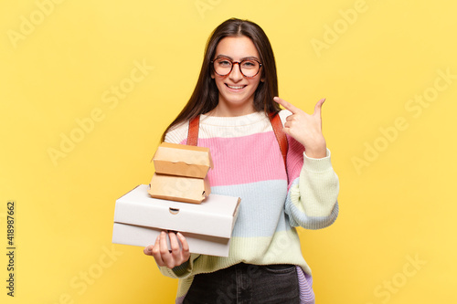 young pretty woman smiling confidently pointing to own broad smile, positive, relaxed, satisfied attitude. take aeay fast food concept photo