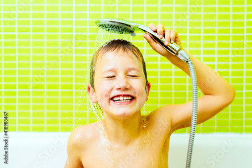 Cuadro en lienzo Boy in the bathtub washes his head with water sprayed from the shower head, with funny expression