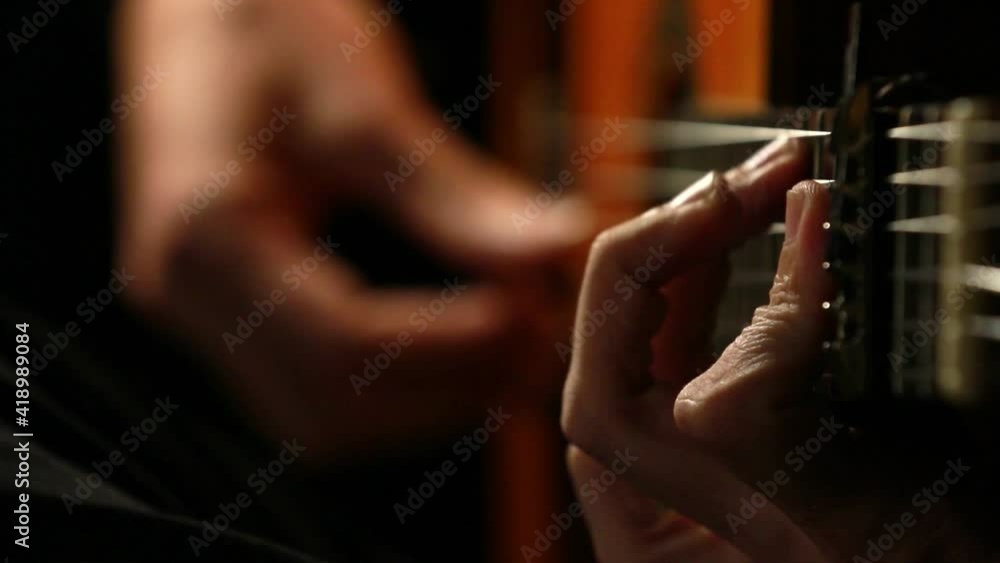 closeup of two hands playing a classical guitar with black background