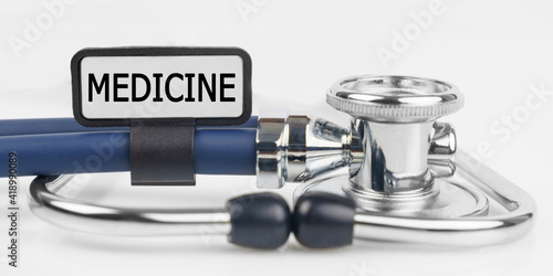 On the white surface lies a stethoscope with a plate with the inscription - MEDICINE