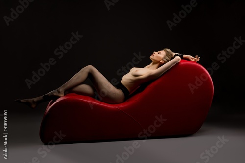 Seductive topless woman lay on red leather sofa