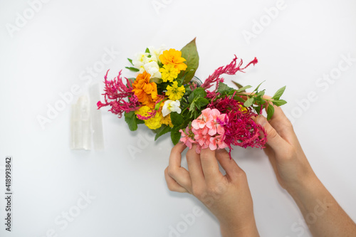 Two hands arranging flowers foraged. White backdrop to hands arranging flowers in a bouquet on top of crystals