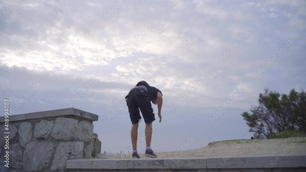 chico caucásico haciendo parkour en la playa en cámara lenta