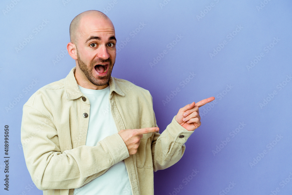 Young caucasian bald man isolated on purple background excited pointing with forefingers away. Young caucasian bald man isolated on purple background excited pointing with forefingers away.