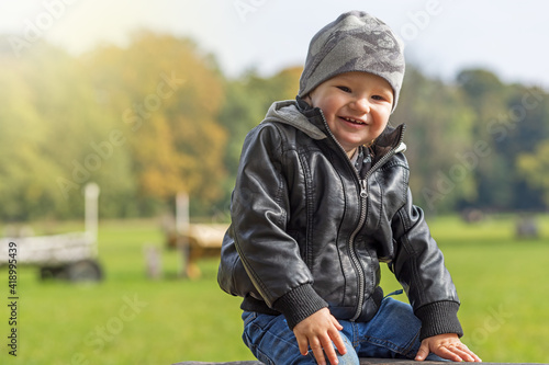 Laughing little boy dressed in a leather jacket is posing in park