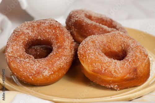 front view, medium distance, of three freshly baked sugar donuts, cooling on a round, yellow plate