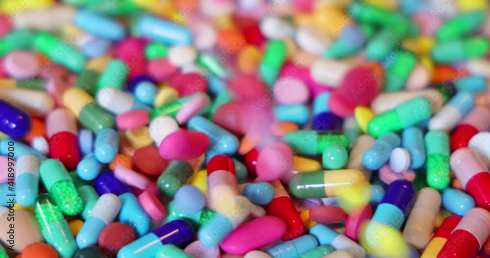 Colorful pills with capsules and tablets falling on white table, concept of medical treatment, slow motion Colorful pills with capsules and tablets falling on white table, concept of medical treatment, slow motion