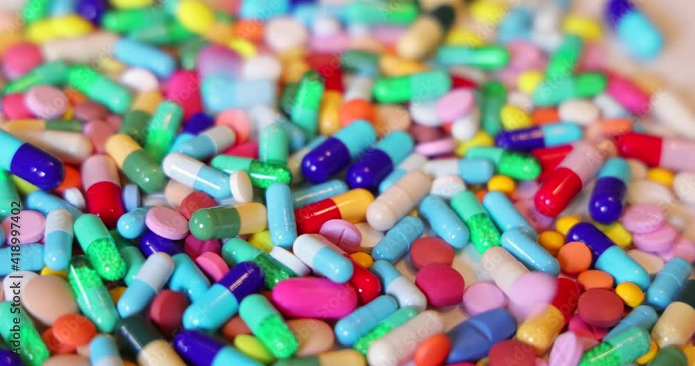 Colorful pills with capsules and tablets falling on white table, concept of medical treatment, slow motion Colorful pills with capsules and tablets falling on white table, concept of medical treatment, slow motion