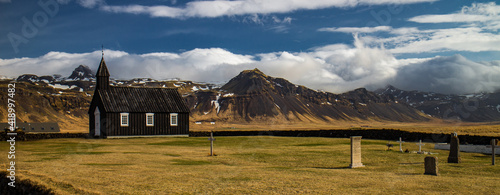 Budir church with cemetary and beautiful mountain landscape with blue sky in background in Iceland