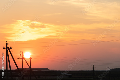 pink sunset over the poles of power lines. A large sun on the horizon line between the wires.