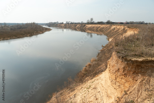 steep high river bank. A wide riverbed or channel. Yellow sand on the shore of an artificial pond.