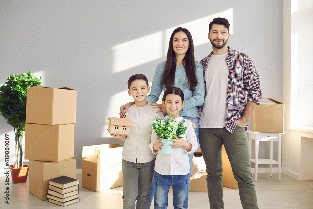 Relocating, new apartment for family concept. Young happy family with children son and daughter standing together in new flat and feeling cheerful with unpacking belongings Relocating, new apartment for family concept. Young happy family with children son and daughter standing together in new flat and feeling cheerful with unpacking belongings
