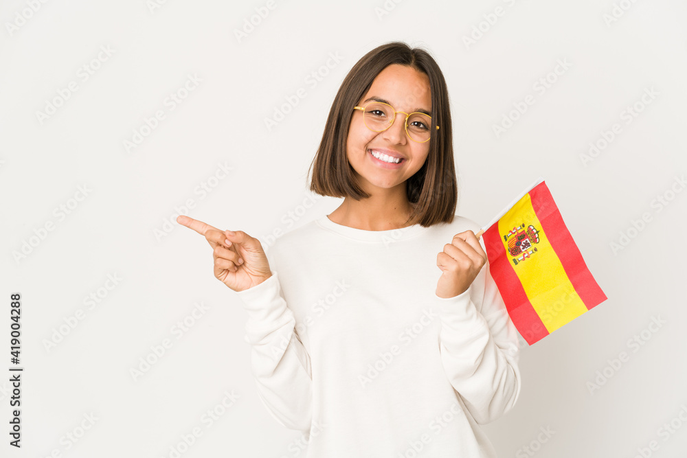 Young hispanic mixed race woman holding a spanish flag smiling and pointing aside, showing something at blank space. Young hispanic mixed race woman holding a spanish flag smiling and pointing aside, showing something at blank space.