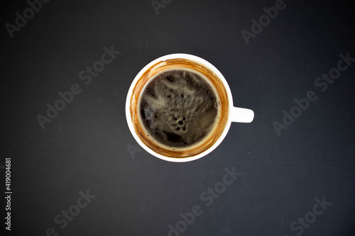 White cup of aromatic freshly ground arabica coffee on a black background. The cup is on the saucer. White cup of aromatic freshly ground arabica coffee on a black background. Top view.
