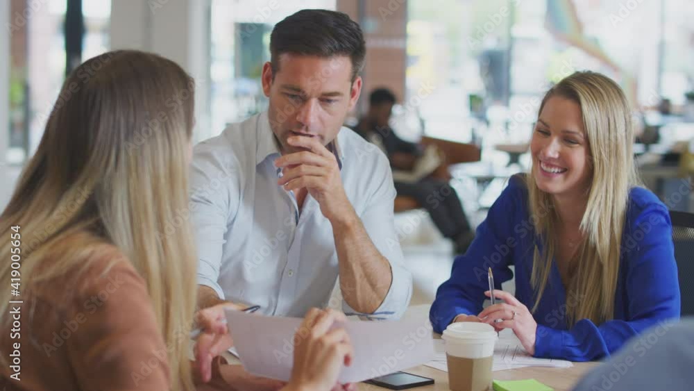 Business team sitting around table in office discussing document together - shot in slow motion Business team sitting around table in office discussing document together - shot in slow motion
