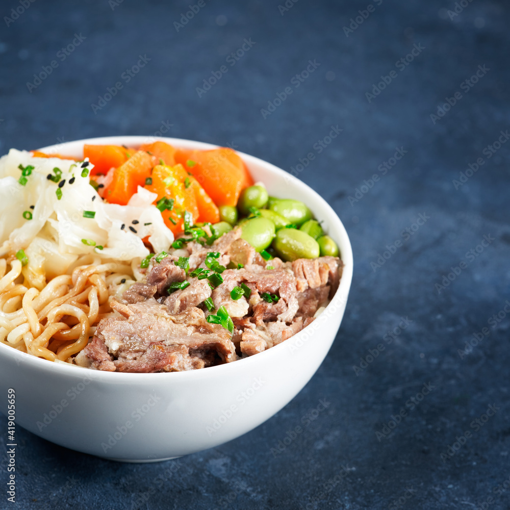 Poke bowl, pulled pork, vegetables, pumkin, soy beans edamame, noodles, on bowl, chopsticks. Copy space, closeup. Hawaiian dish, blue dark background. Trendy asian food. Healthy, clean eating concept. Poke bowl, pulled pork, vegetables, pumkin, soy beans edamame, noodles, on bowl, chopsticks. Copy space, closeup. Hawaiian dish, blue dark background. Trendy asian food. Healthy, clean eating concept.