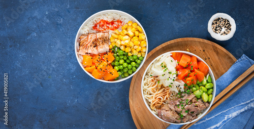 Food banner, two assorted poke bowls, flamed salmon, pulled pork, vegetables, rice, sauces. Top view, closeup. Hawaiian dish, blue dark background. Trendy asian food. Healthy and clean eating concept.