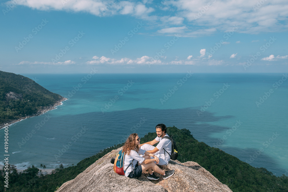 A couple stand on a rock at a viewpoint with an epic view of the ocean