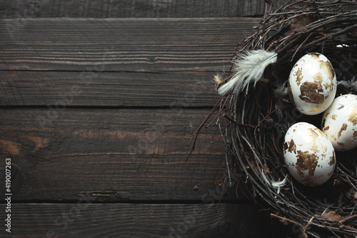 easter golden eggs in a nest on a dark wooden background with place for text, top view