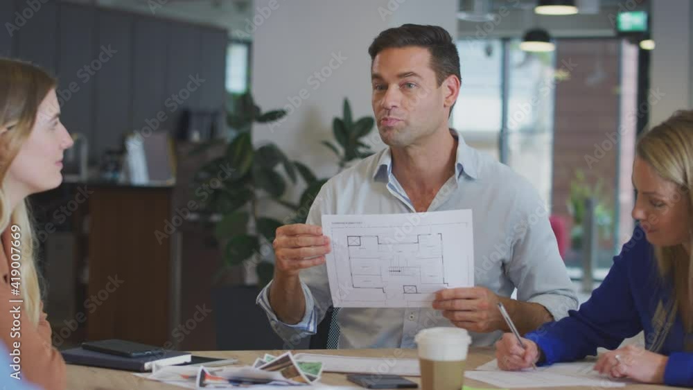 Business team in architects practise sitting around table in office discussing plan together - shot in slow motion Business team in architects practise sitting around table in office discussing plan together - shot in slow motion