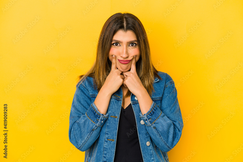 Young indian woman isolated on yellow background doubting between two options. Young indian woman isolated on yellow background doubting between two options.