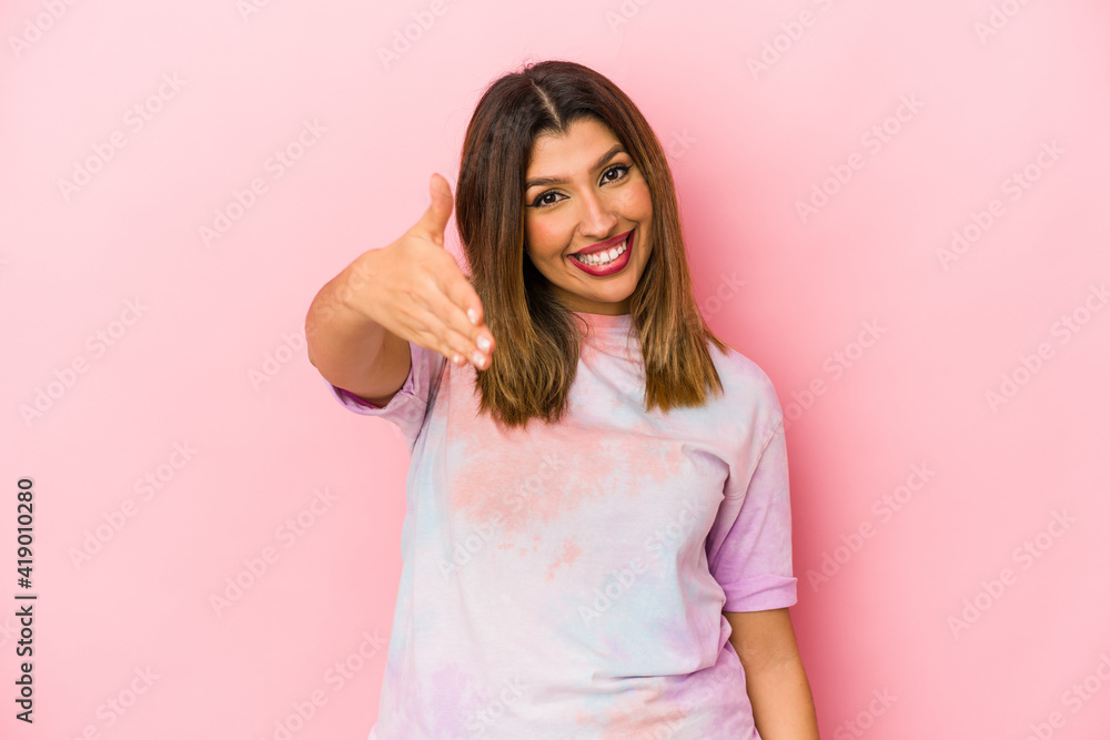 Young indian woman isolated on pink background stretching hand at camera in greeting gesture. Young indian woman isolated on pink background stretching hand at camera in greeting gesture.