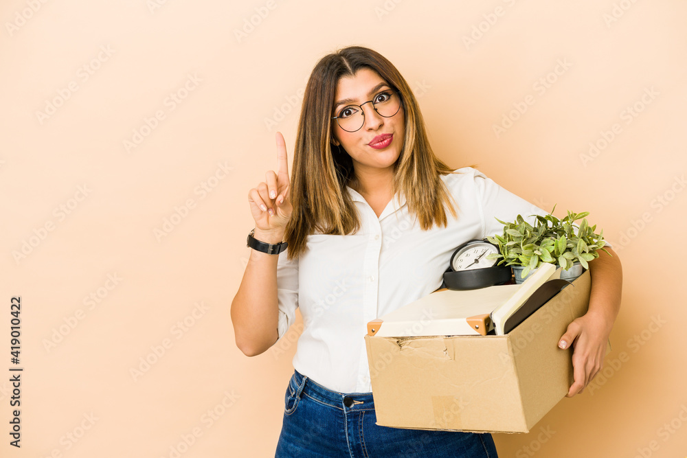 Young indian woman moving holding a box isolated showing number one with finger. Young indian woman moving holding a box isolated showing number one with finger.