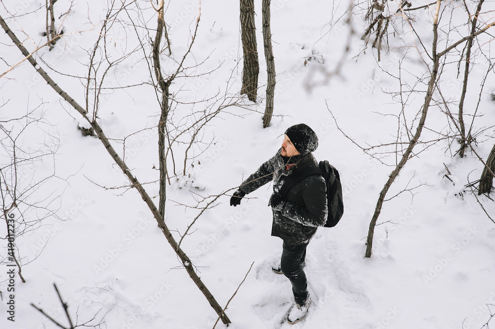 A wanderer, a tourist in black clothes and a large backpack, walks through the snowy forest in winter. Photography, concept.